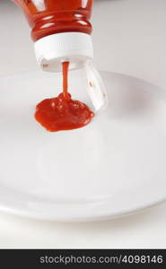 Bottle of ketchup pouring out onto a white plate.