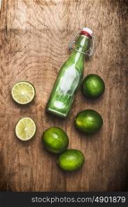 Bottle of Lime juice with fresh lime fruits on rustic wooden background, top view, copy space