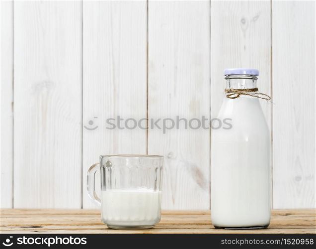 Bottle of milk and half full glass with milk on a wooden vintage table, white wooden background with copy space. Fresh milk, reusable glassware, healthy nutrition. Bottle of milk and half full glass with milk on a wooden table