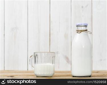 Bottle of milk and half full glass with milk on a wooden vintage table, white wooden background with copy space. Fresh milk, reusable glassware, healthy nutrition. Bottle of milk and half full glass with milk on a wooden table