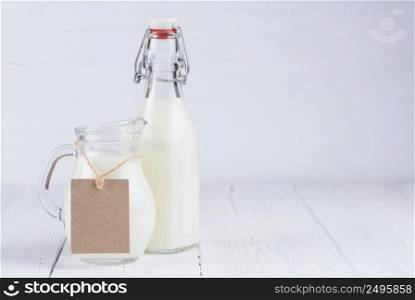 Bottle of milk and jar of milk with blank cardboard label, on white wooden table