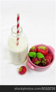 Bottle of milk and pink cup with fresh strawberries, focus on the milk
