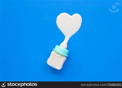 Bottle of milk for baby on blue background. Milk heart shape, Top view