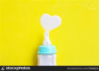 Bottle of milk for baby on yellow background. Milk heart shape, Top view