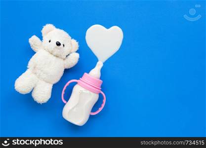 Bottle of milk for baby with toy white bear on blue background. Copy space