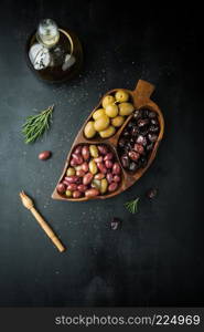 Bottle of olive oil, assorted of marinated olives with herbs and rosemary on a dark background
