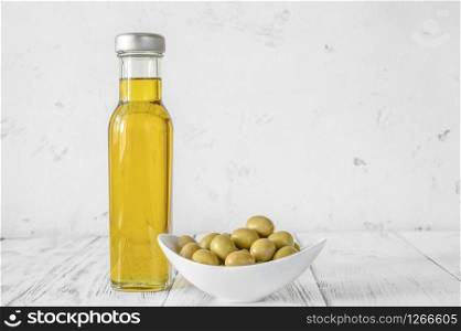 Bottle of olive oil with green olives on wooden background