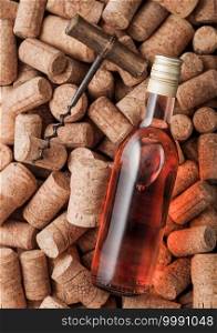 Bottle of pink rose wine and vintage corkscrew on top of various wine corks background.