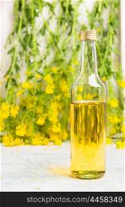 Bottle of rapeseed oil on white wooden table over fresh rape flowers