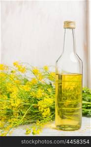 bottle of rapeseed oil with lower of a rape on white wooden background