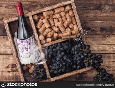 Bottle of red wine and empty glass with dark grapes with corks and opener inside vintage wooden box on grunge wooden background with linen towel.