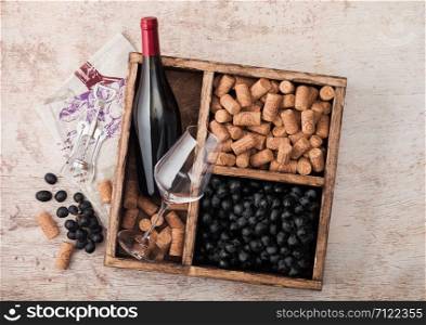 Bottle of red wine and empty glass with dark grapes with corks and opener inside vintage wooden box on wooden background with linen towel.