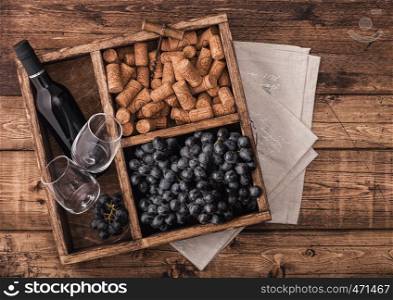 Bottle of red wine and empty glasses with dark grapes with corks and opener inside vintage wooden box on grunge wooden background with linen towel.