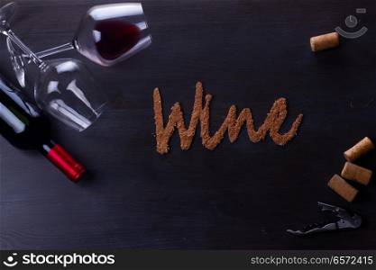 Bottle of red wine and two wine glasses on table with wine word letters. Glass of red wine
