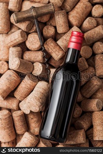 Bottle of red wine and vintage corkscrew on top of various wine corks background.