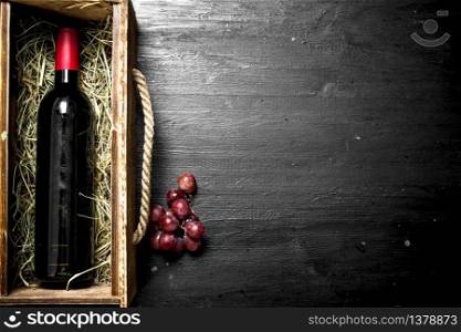 bottle of red wine in an old box with a branch of grapes. On the black chalkboard.. bottle of red wine in an old box with a branch of grapes.