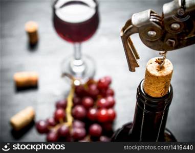 Bottle of red wine with a corkscrew. On a black wooden background.. Bottle of red wine with a corkscrew.