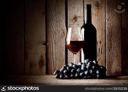 Bottle of red wine with a glass and grapes on a wooden background