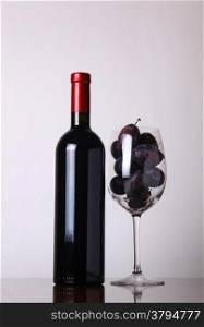 Bottle of red wine with a glass filled with plums over a white background
