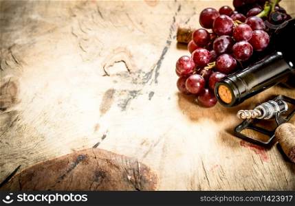 Bottle of red wine with a sprig of grapes and a corkscrew. On wooden background.. Bottle of red wine with grapes