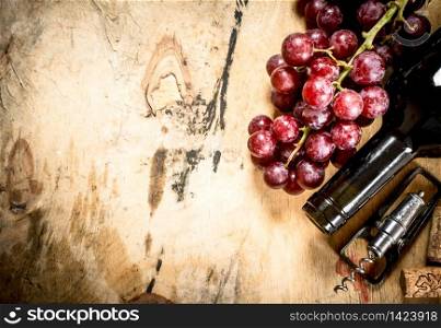 Bottle of red wine with a sprig of grapes and a corkscrew. On wooden background.. Bottle of red wine with grapes