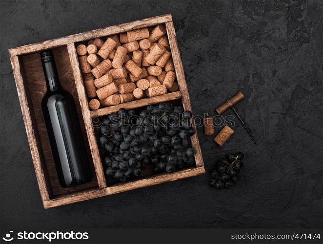 Bottle of red wine with dark grapes with corks and opener inside vintage wooden box on black background.