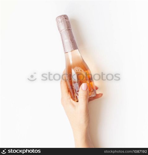 Bottle of rose champagne wine in woman hand in minimal composition isolated on white background with copy space. Natural light. Template for tasting, degustation invitation card. Top view. Flat lay