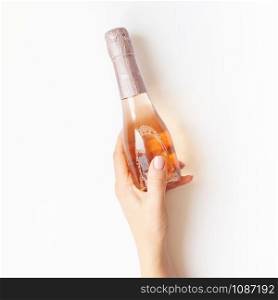Bottle of rose champagne wine in woman hand in minimal composition isolated on white background with copy space. Natural light. Template for tasting, degustation invitation card. Top view. Flat lay