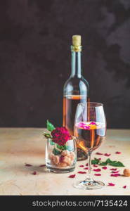 Bottle of rose wine and glass served with rose wine and rose petals, rose and candied fruit in glass on pink concrete table and dark background. Beautiful valentine or wedding greeting card.