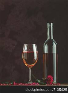 Bottle of rose wine and glass served with rose wine and rose petals, pink rose on dark background. Beautiul valentine or wedding greeting card.