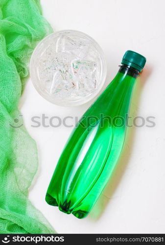 Bottle of sparkling mineral water with glass of ice and green cloth on white background