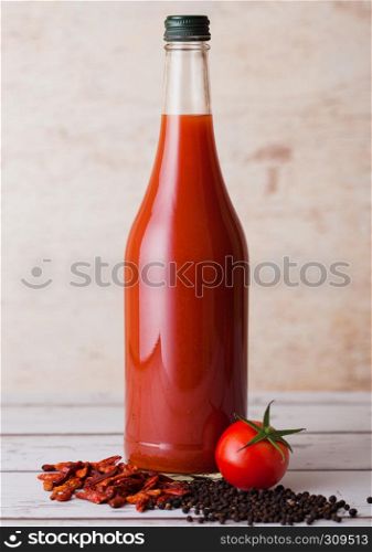 Bottle of spicy tomato juice with red and black pepper on wooden background