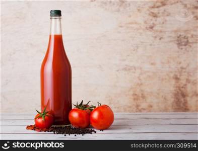 Bottle of spicy tomato juice with red and black pepper on wooden background