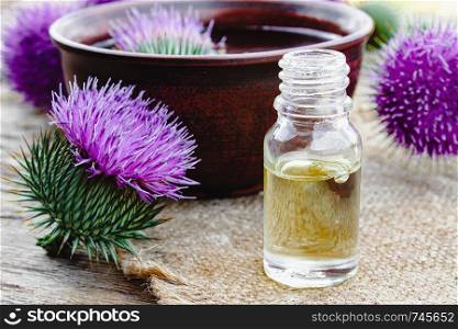 Bottle of thistle essential oil with thistle flowers on wooden background. Close-up. Bottle of thistle essential oil with thistle flowers on wooden background.