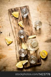 Bottle of vodka with shot glasses and lemon. On wooden background.. Bottle of vodka with shot glasses and lemon.