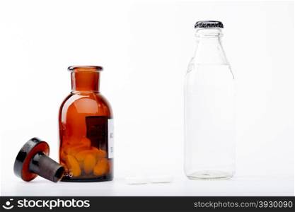 Bottle of water, a glass medicine bottle and white pills on white background