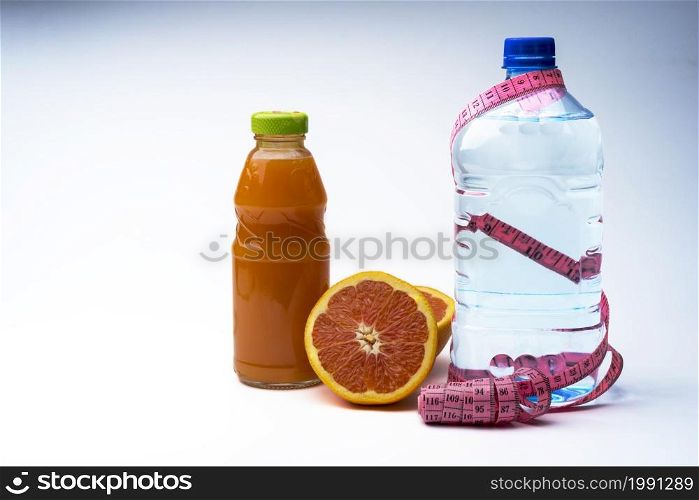 Bottle of water with centimeter and grapefruit juice from fresh grapefruit on grey background. The concept of healthy eating, fat burning.. Bottle of water with centimeter and grapefruit juice from fresh grapefruit on grey background.