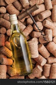 Bottle of white wine and vintage corkscrew on top of various wine corks background.