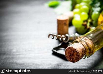 bottle of white wine with a corkscrew. On a black wooden background.. bottle of white wine with a corkscrew.