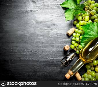 bottle of white wine with branches of grapes. On a black wooden background.. White fresh wine