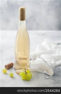 Bottle of white wine with grapes and empty glass on light background.