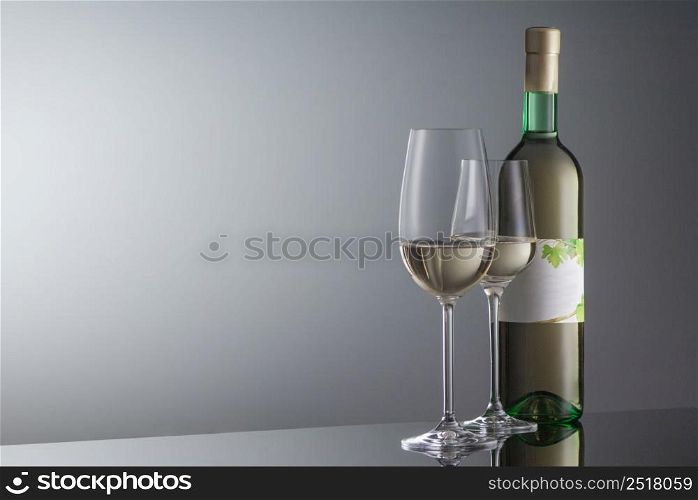 bottle of white wine with wineglass on grey background with illumination. a bottle of alcoholic drink