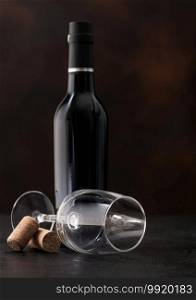 Bottle of wine and empty classic wine glass with corks on dark background.
