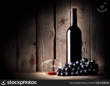 Bottle of wine, glass and inverted bunch grapes on a wooden background