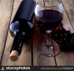 Bottle of wine, glass of red wine and grapes. bottle of wine filled with a glass and grapes on an old wooden table.