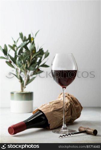 Bottle of wine in shopping paper bag with opener and glass of wine.