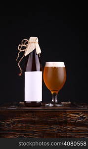 Bottle with blank label template and glass of home brewed craft beer standing on a wooden chest