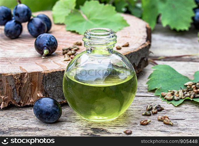 Bottle with grape seed essential oil on old wooden boards near grones of blue grapes and green leaves. Spa, bio, eco products concept.. Bottle with grape seed essential oil on old wooden boards near grones of blue grapes and green leaves. Spa, eco products concept.