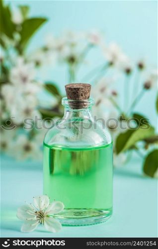 Bottle with natural cosmetic oil and flowers on a blue background. Aromatherapy and spa wellness concept. Organic skin care product.. Bottle with natural cosmetic oil and flowers on blue background. Aromatherapy and spa wellness concept. Organic skin care product.