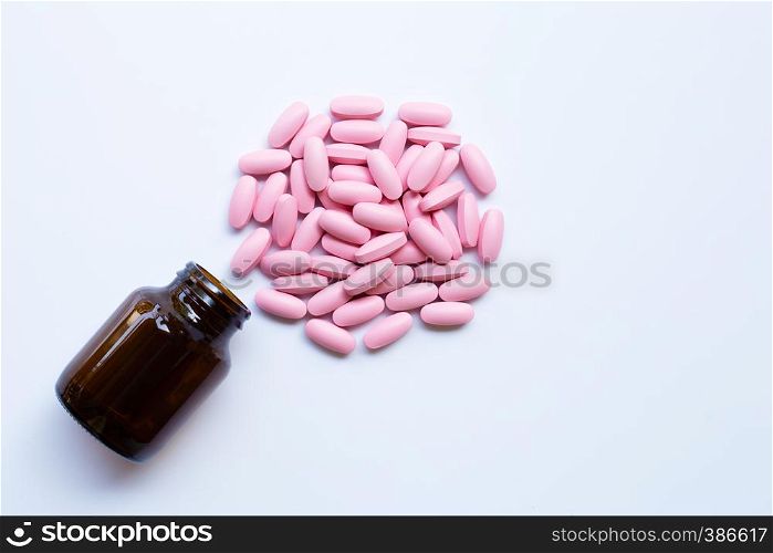 Bottle with pink medicine pills on white